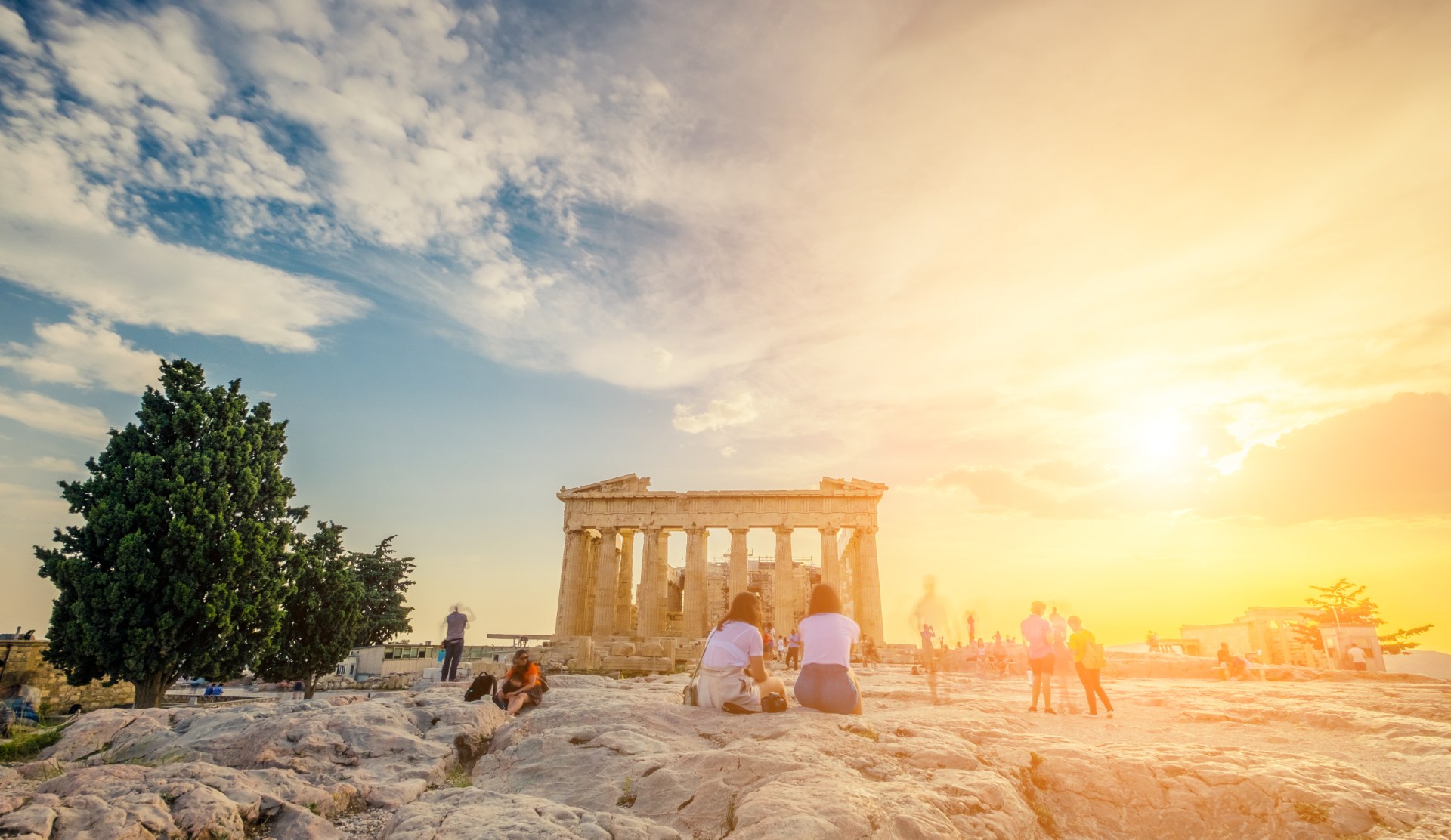 Des jeunes assis devant le Parthénon, sur l’Acropole, au coucher du soleil